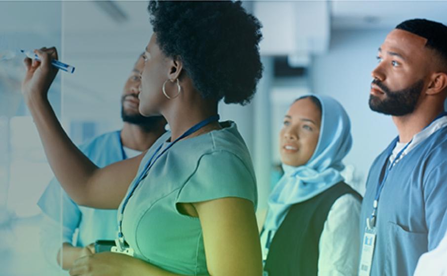 A woman is writing on a white board with a dry erase marker as three individuals in the background watch.