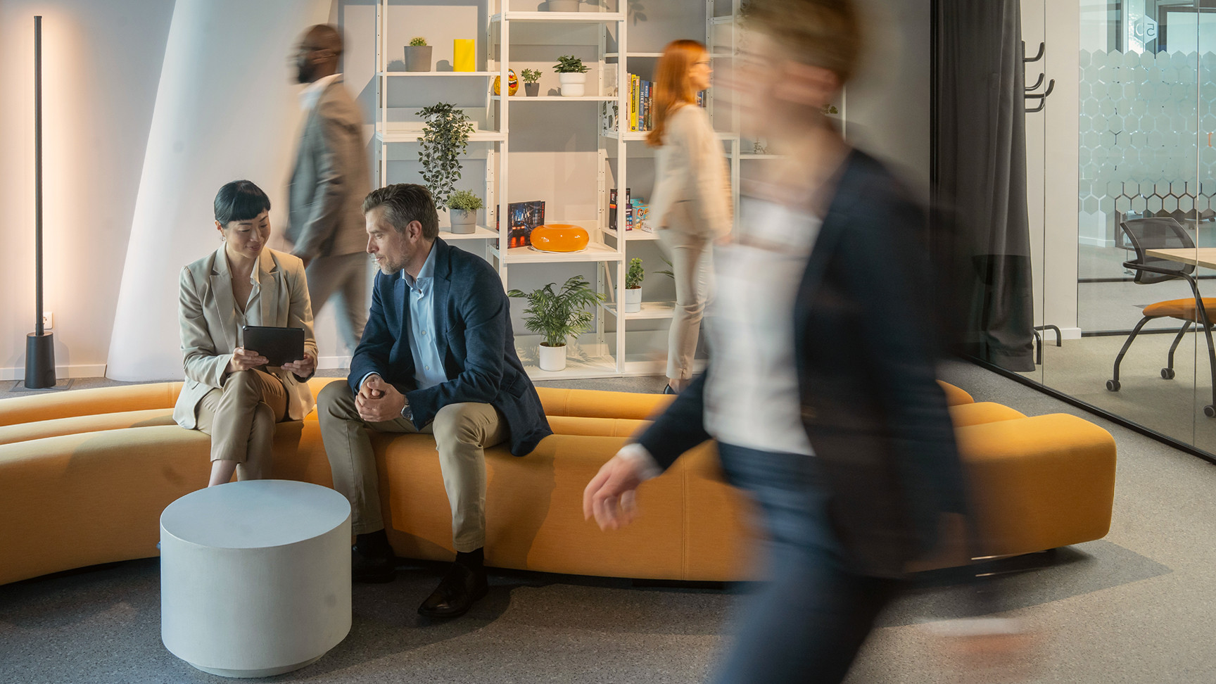 A man and woman on a bench in an open area of an office looking at an electronic tablet
